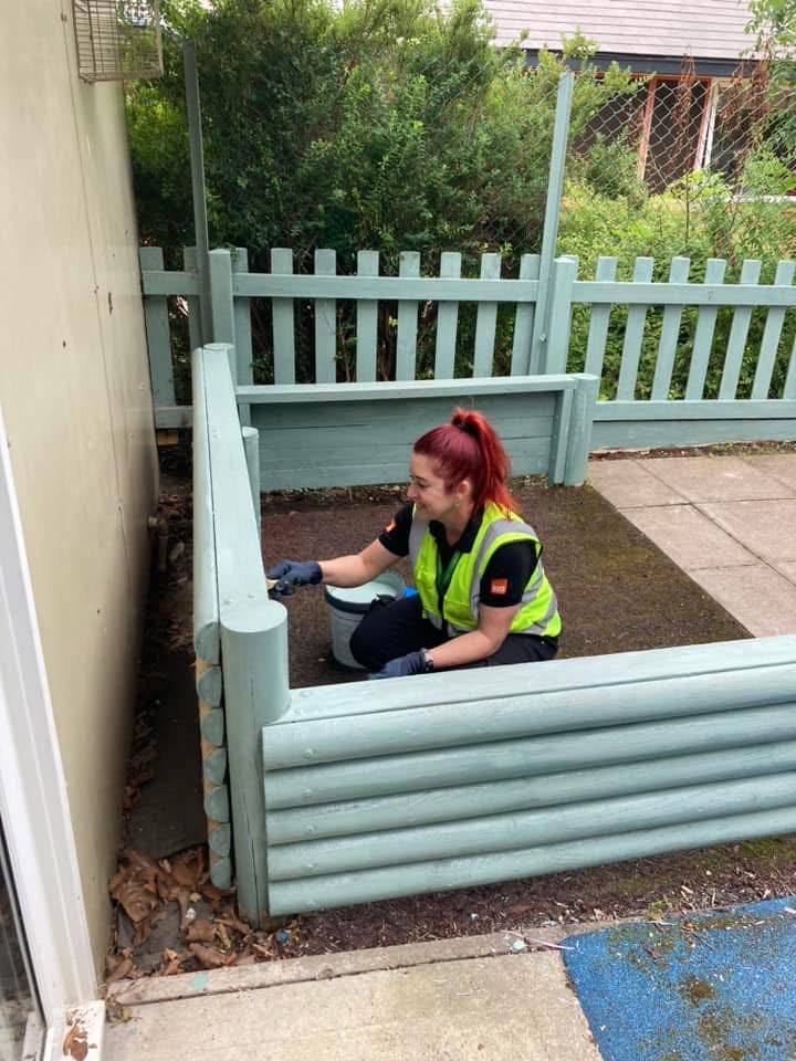 Lady in B&Q uniform painting a wooden bench